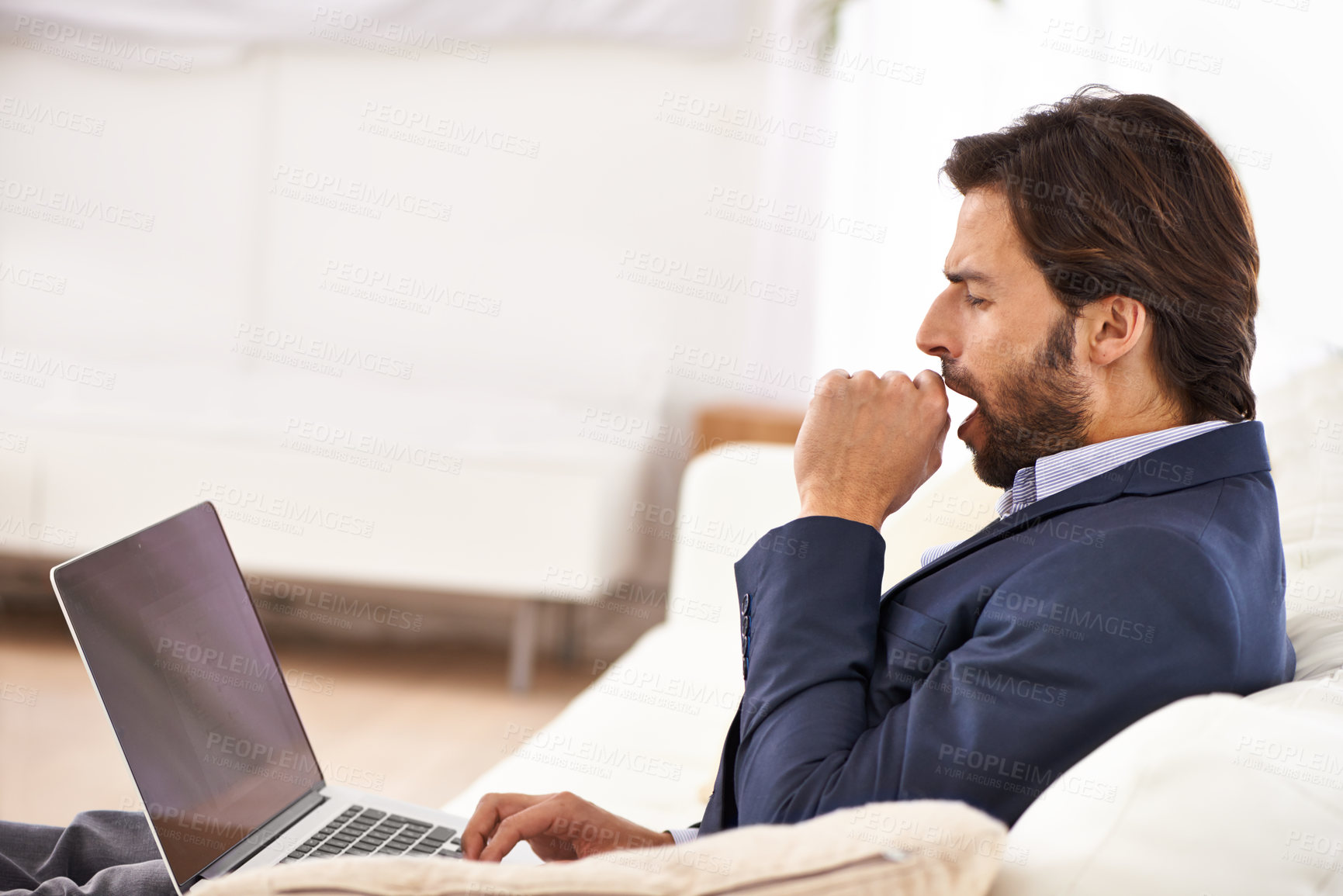 Buy stock photo A handsome businessman yawning while working on his laptop