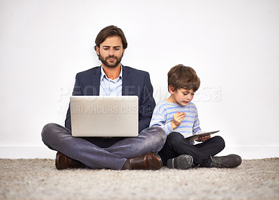 Buy stock photo A father and son sitting on the floor against a wall with a laptop and digital tablet