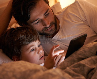 Buy stock photo A father and son lying in bed with an e-reader