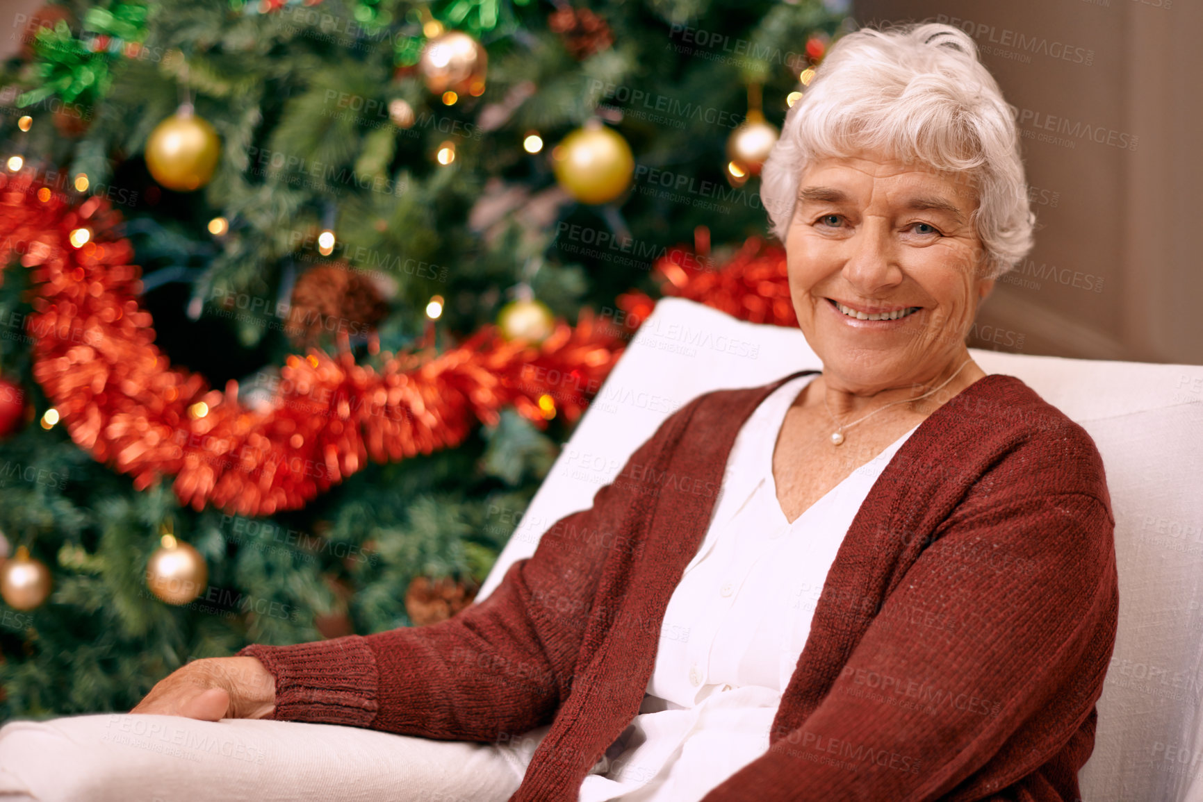 Buy stock photo A happy senior woman sitting on a couch with a Christmas tree behind her