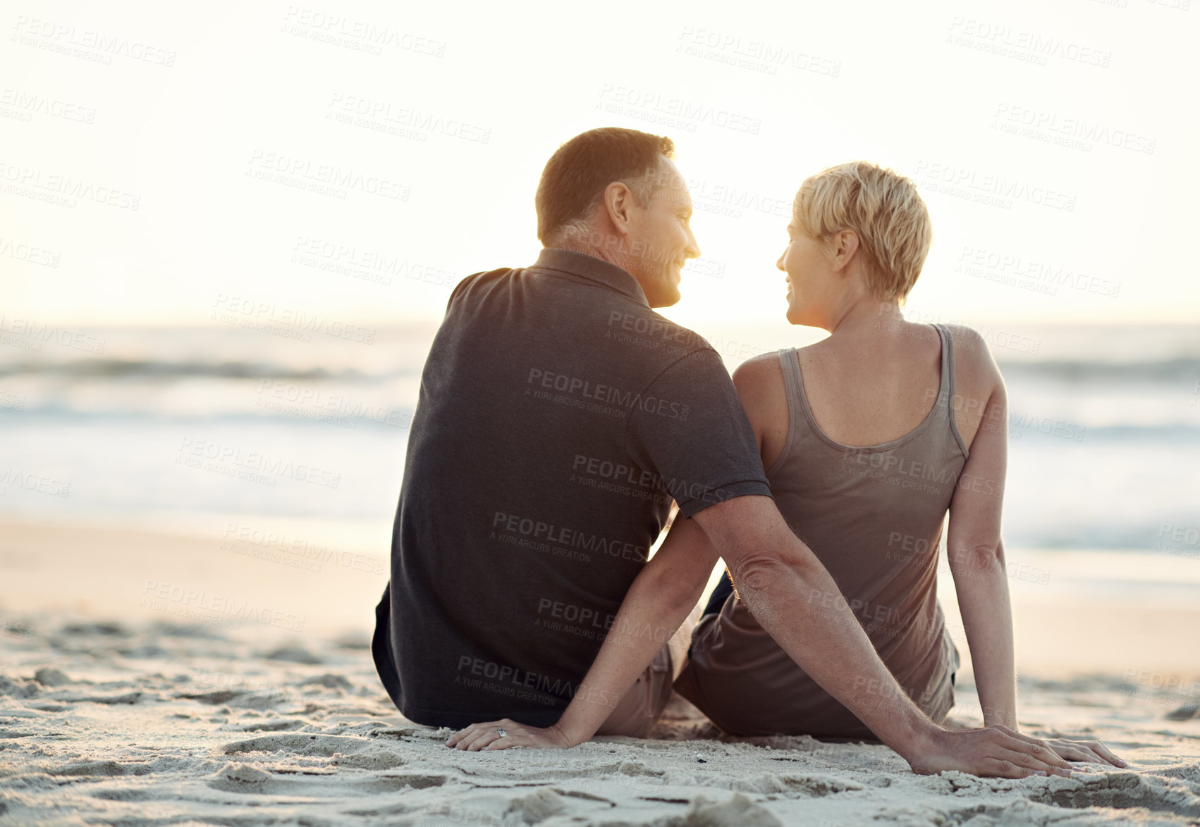 Buy stock photo A loving couple sitting on the beach - rear view
