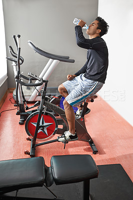 Buy stock photo Exercise bike, man and drinking water in a gym, fitness and endurance with nutrition and progress. Workout, bodybuilder and person with a bottle and wellness with cycling and cardio with a challenge