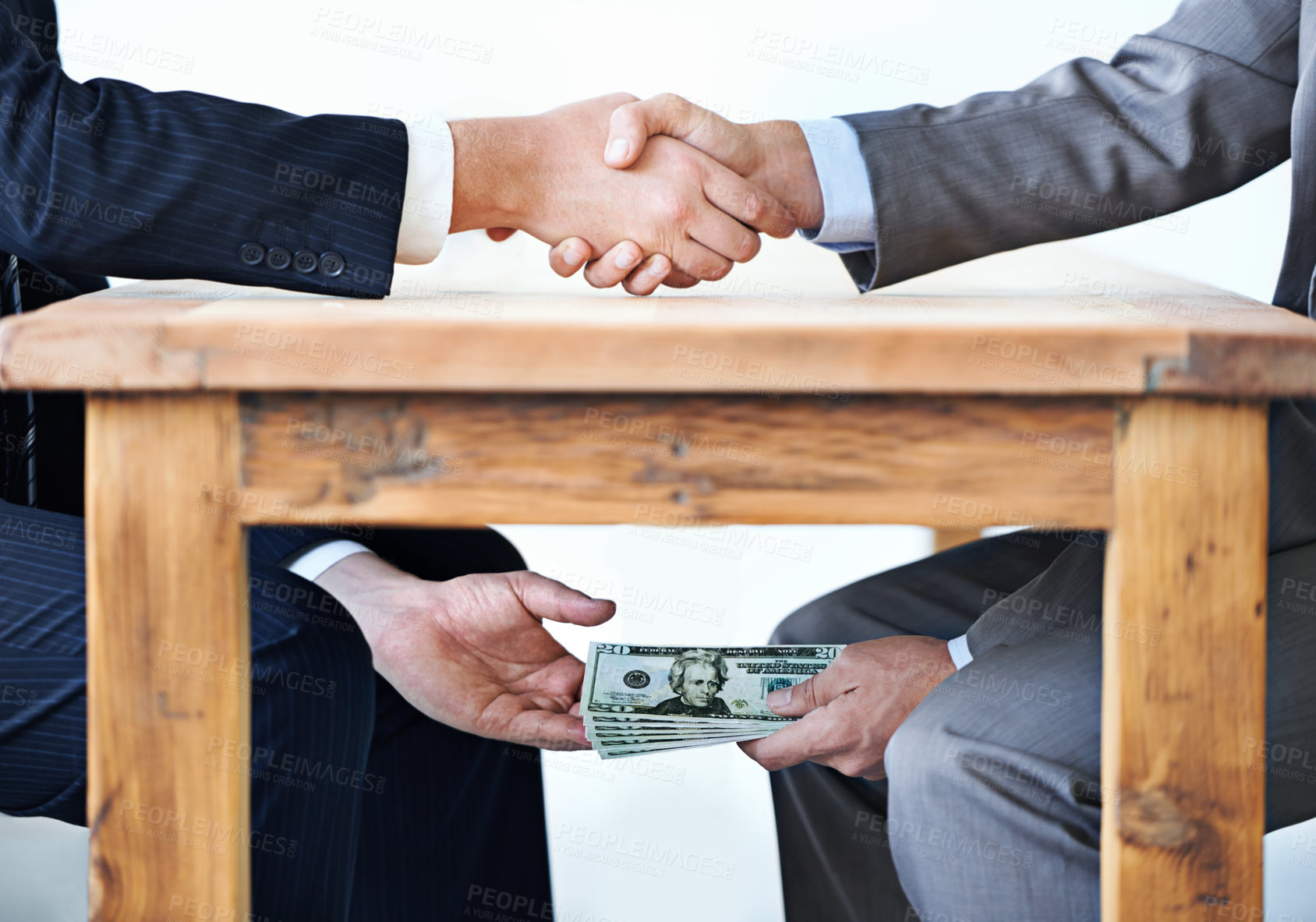 Buy stock photo Cropped shot of two businessmen shaking hands while money passes hands under a table