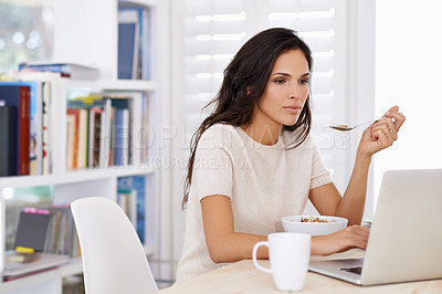 Buy stock photo Shot of a busy young woman eating breakfast while surfing the net