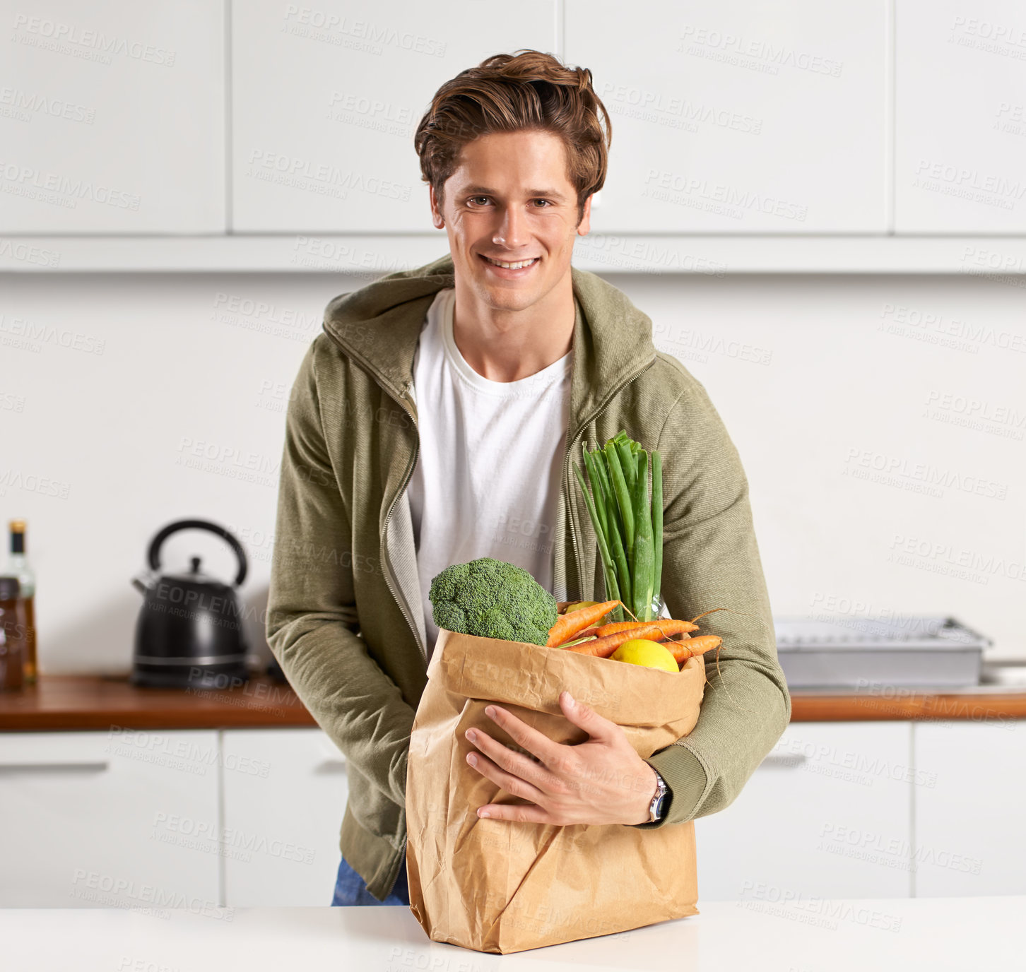 Buy stock photo A young man in a kitchen holding a brown paper bag filled with vegetables