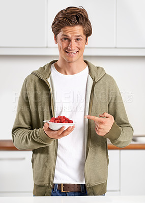 Buy stock photo A handsome young man pointing to a bowl of raspberries