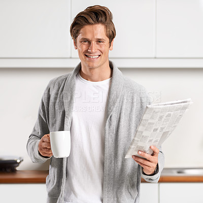 Buy stock photo A young man standing in a kitchen drinking coffee and reading the newspaper