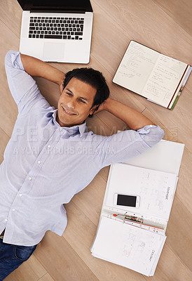 Buy stock photo High angle shot of a young businessman lying on his home floor surrounded by work