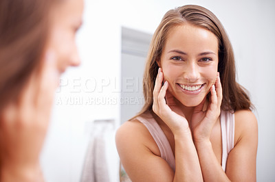 Buy stock photo A young woma touching her face happily as she looks in the mirror