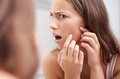Buy stock photo A young woman looking shocked as she examines her skin