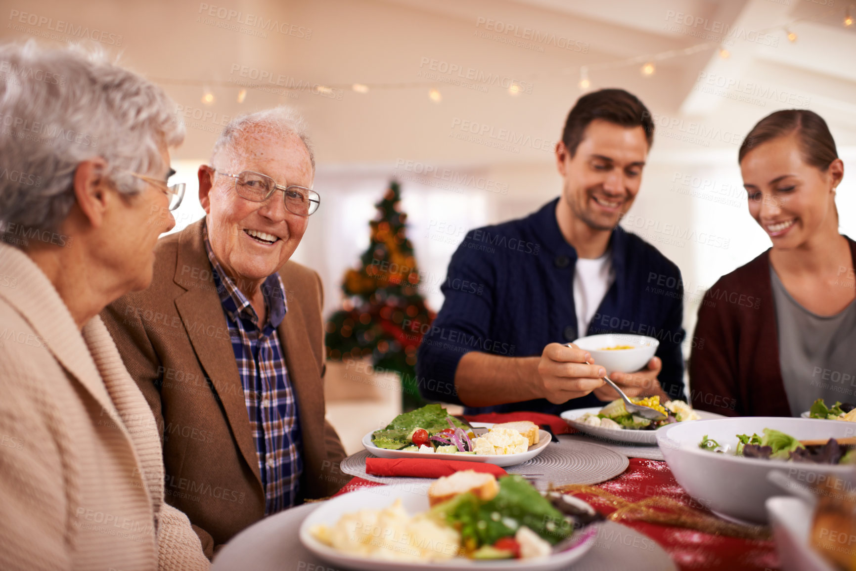 Buy stock photo Christmas, happy family and eating lunch in home, smile and bonding together at party. Xmas, food and senior parents at table for festive celebration, relax and people on holiday with salad for meal