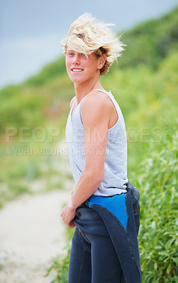 Buy stock photo Shot of a young surfer pulling on his wetsuit