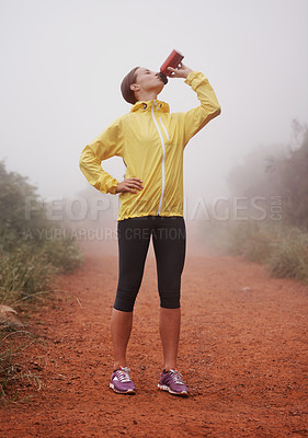 Buy stock photo A young female runner drinking from her water bottle while standing in a forest trail