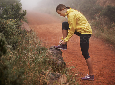 Buy stock photo A young female runner tying her shoelaces while out training