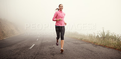 Buy stock photo Shot of a young woman jogging on a country road on a misty morning