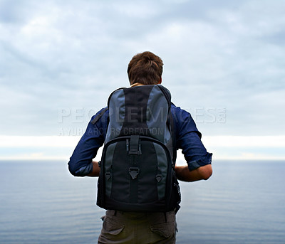 Buy stock photo Man, backpack and hiking by ocean for travel, sightseeing or outdoor journey in nature. Rear view of male person, hiker or tourist with bag on back for trekking, fitness or adventure with cloudy sky