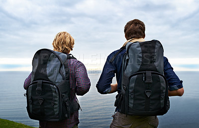 Buy stock photo Couple, backpack and hiking by ocean for travel, sightseeing or outdoor journey in nature. Rear view of man, woman or hikers carrying bag on back for trekking, fitness or adventure with cloudy sky