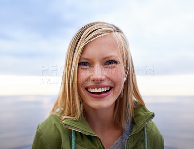 Buy stock photo Woman, excited and smile at the beach for holiday, vacation and travel in winter portrait. Face of a young person from the USA and happy by an ocean, sea or lake with cloudy sky for outdoor adventure