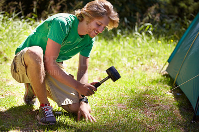 Buy stock photo Man, smile and tent with hammer at campsite for setting up in grass of nature, park and environment. Male person, working and happy with job, rope and outdoor for adventure in summer holiday