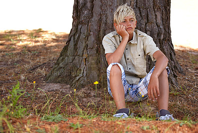 Buy stock photo Boy, bored and depression by tree with anxiety, mental health or stress on grass in nature. Young male person, child or teenager resting on break by wood stump in loneliness, childhood or left out