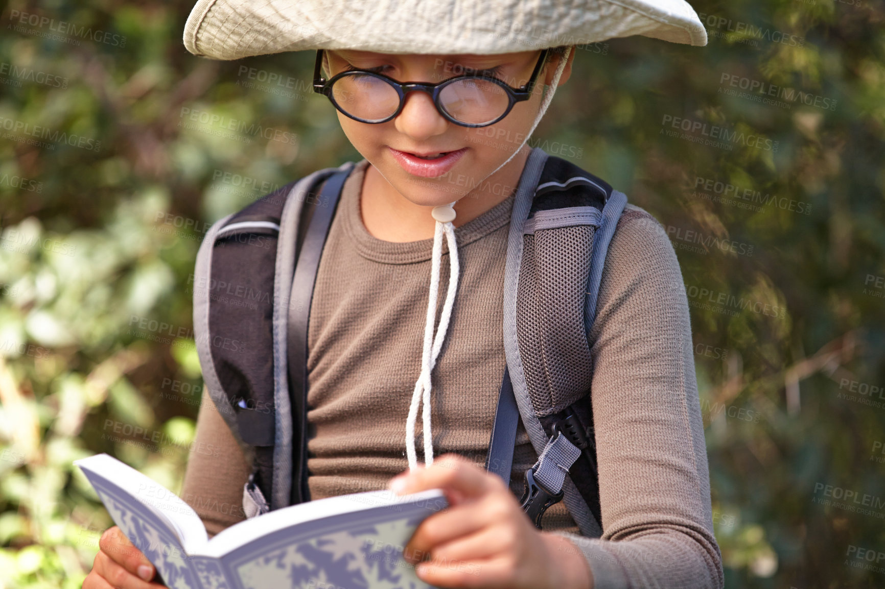 Buy stock photo Happy, little boy and reading book in forest for travel guide, adventure or outdoor discovery. Male person, child or kid with glasses, hat and notebook for story, exploration or research in nature