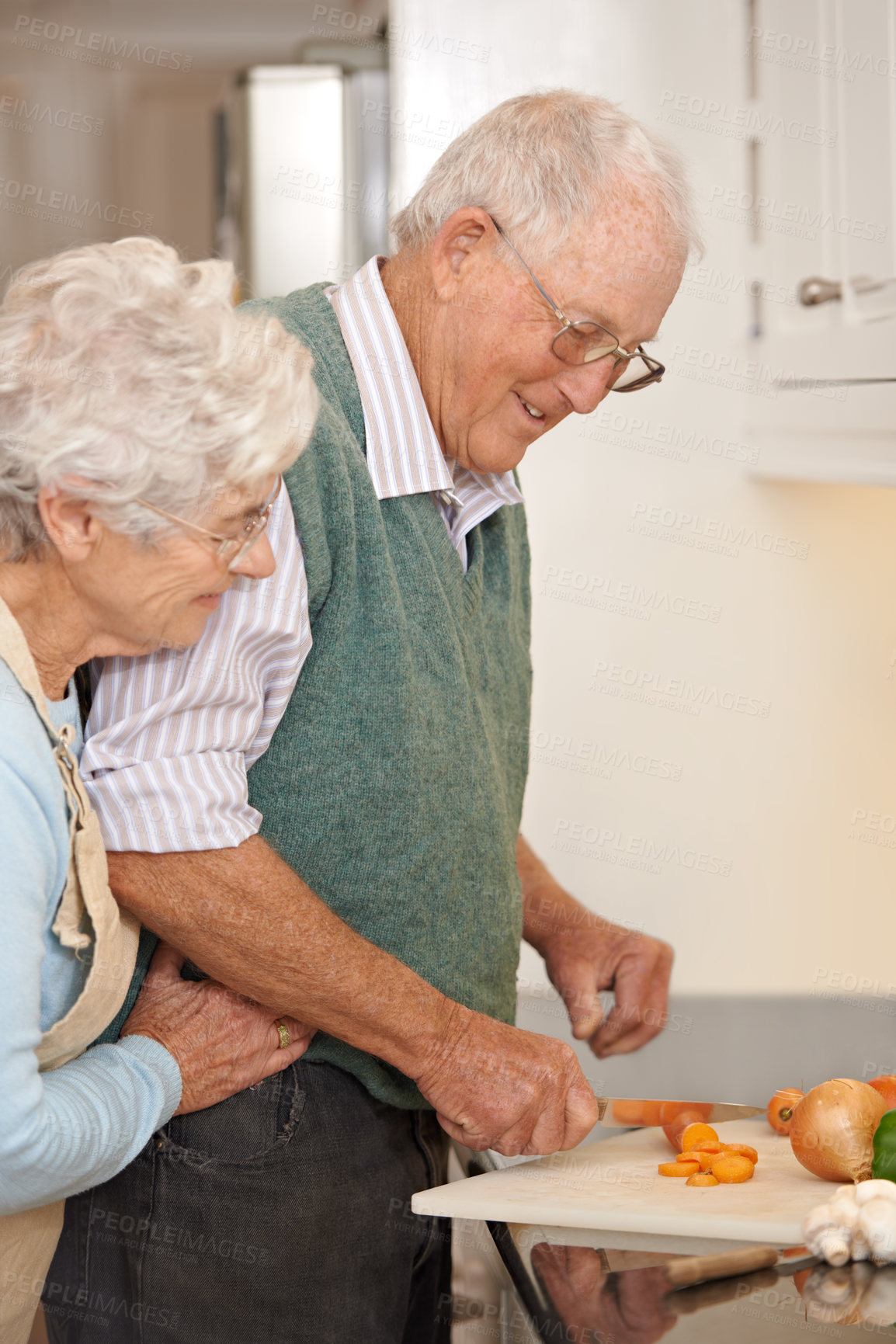 Buy stock photo Senior couple, cutting vegetables and embrace in kitchen, food preparation and love at home. Elderly people, healthy meal and organic ingredients for nutrition, hug and diet for detox in retirement