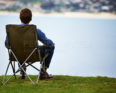 Buy stock photo Rear-view of a young man sitting on a camping chair and looking at the view