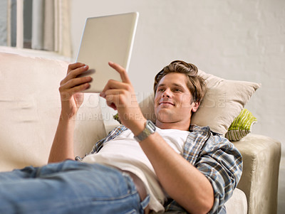 Buy stock photo Tablet, relax and man on sofa in home for social media, networking and browse website. Happy, smile and person lying on couch with digital tech for internet, connection and streaming in living room