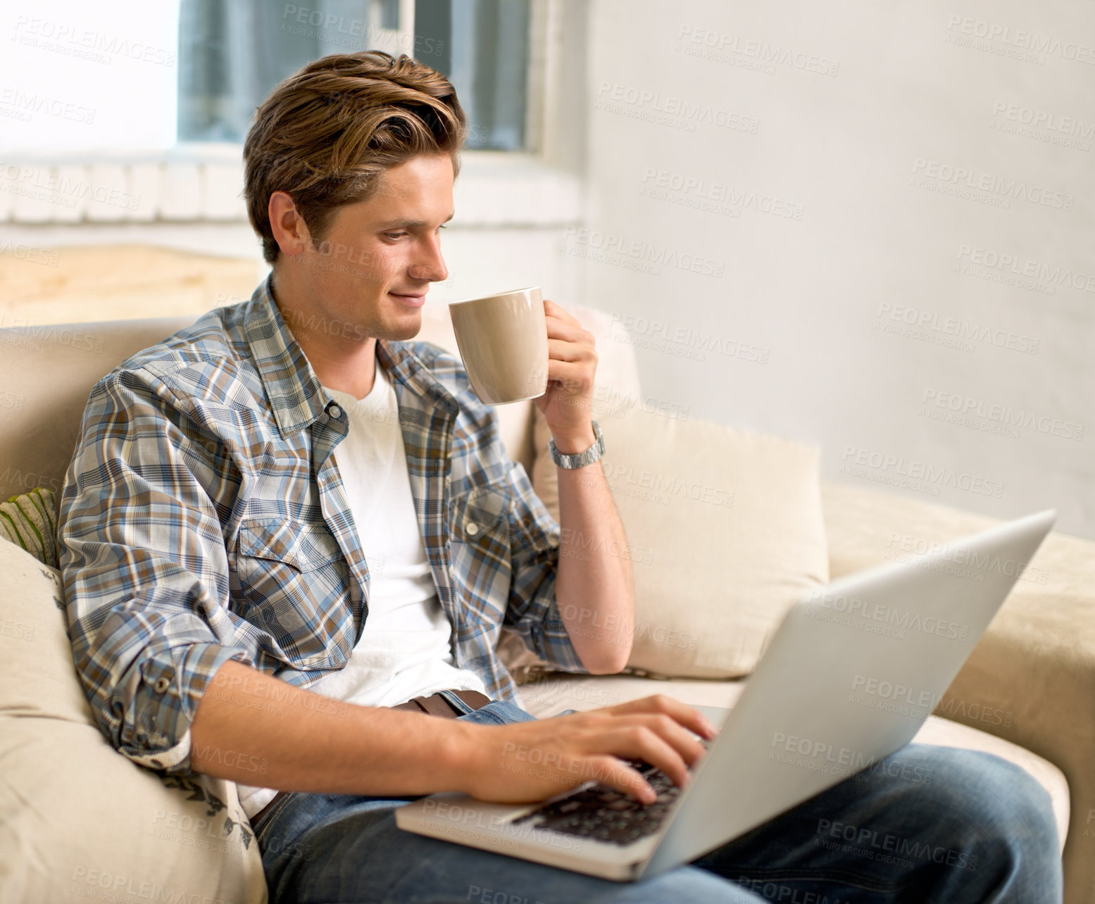 Buy stock photo Shot of a handsome young man using his laptop while having coffee at home