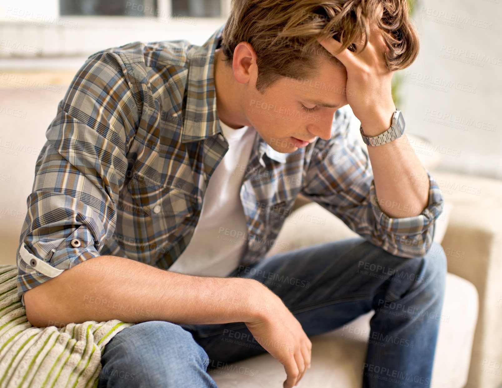 Buy stock photo A young man sitting on a couch with his hand in his hair as if in pain