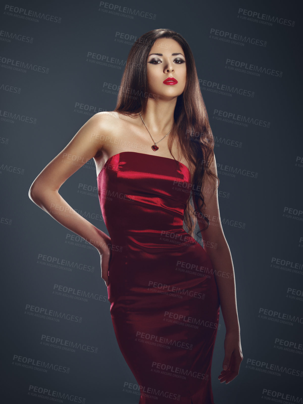 Buy stock photo Fashion model posing sensually in a fitting red satin dress against a dark background