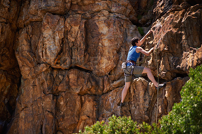 Buy stock photo A wide shot of a young woman rock climbing