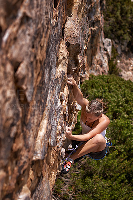 Buy stock photo Shot of a young woman climbing up a mountain rockface