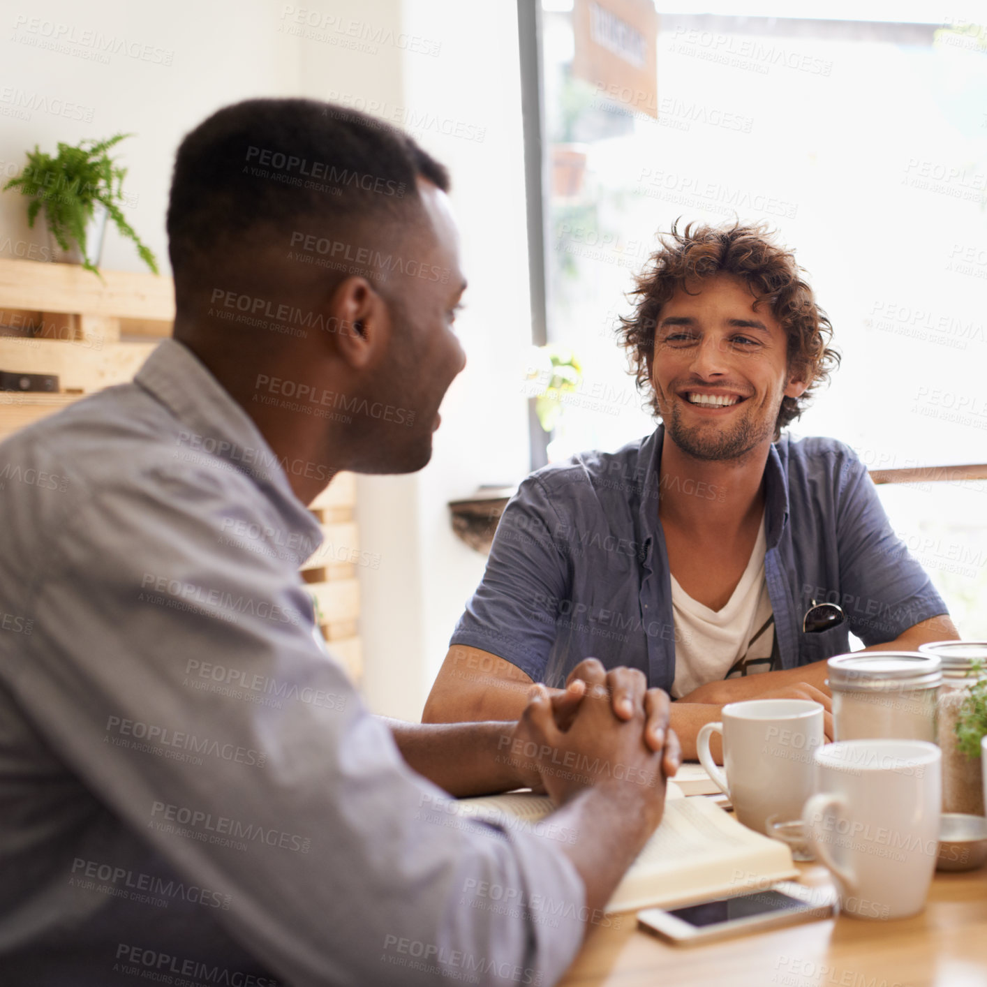 Buy stock photo Two young men having a conversation while having coffee at a cafe