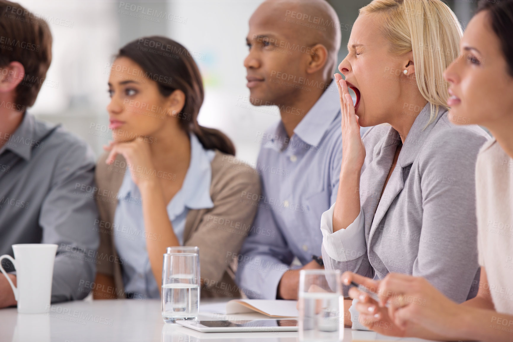 Buy stock photo Shot of a businesswoman yawning during a meeting with her colleagues