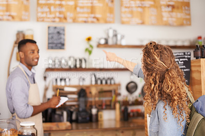 Buy stock photo Woman, coffee shop and pointing at menu on wall with barista, notes and service for good customer experience. Male waiter writing, lady and talking with choice, decision and order from bakery shop
