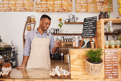 Buy stock photo Man, coffee shop and phone of a waiter with happiness from small business. Cafe, mobile and African barista entrepreneur looking on online order app with  smile at bakery and restaurant feeling happy