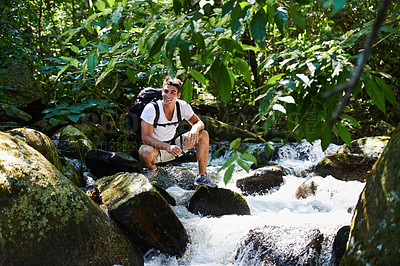 Buy stock photo Man, hiking and river in tropical rainforest with smile for adventure, journey and rocks with backpack. Person, outdoor and bag by water, earth and trees in jungle on holiday with freedom in Colombia