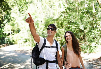 Buy stock photo Happy couple, backpack and pointing with direction in forest for hiking, adventure or outdoor journey in nature. Young man and woman holding hands with bag for trekking, sightseeing or destination