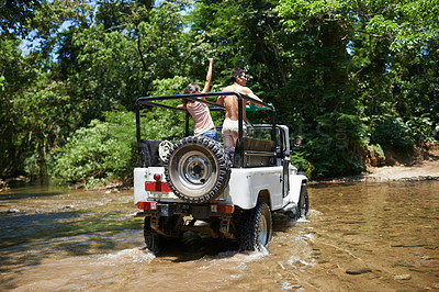 Buy stock photo Shot of a young couple driving through a river in their off-road vehicle