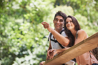 Buy stock photo Couple, point and backpack for hiking in forest with smile for thinking, holiday or search by trees. Man, woman and bag for trekking, direction or journey in jungle on bridge for vacation in Colombia