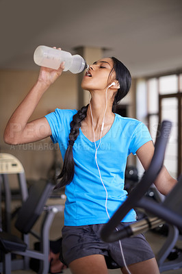 Buy stock photo Woman, drinking water and bike in gym, cycling and stationary machine for workout at club. Female person, earphones and hydrate for strength training, music and equipment for fitness and body health