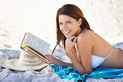 Buy stock photo Beach, portrait and woman reading book to relax in summer on towel, sand and outdoor in nature. Girl, smile and happiness in bikini at sea, vacation and hat for sun, weekend and novel for person