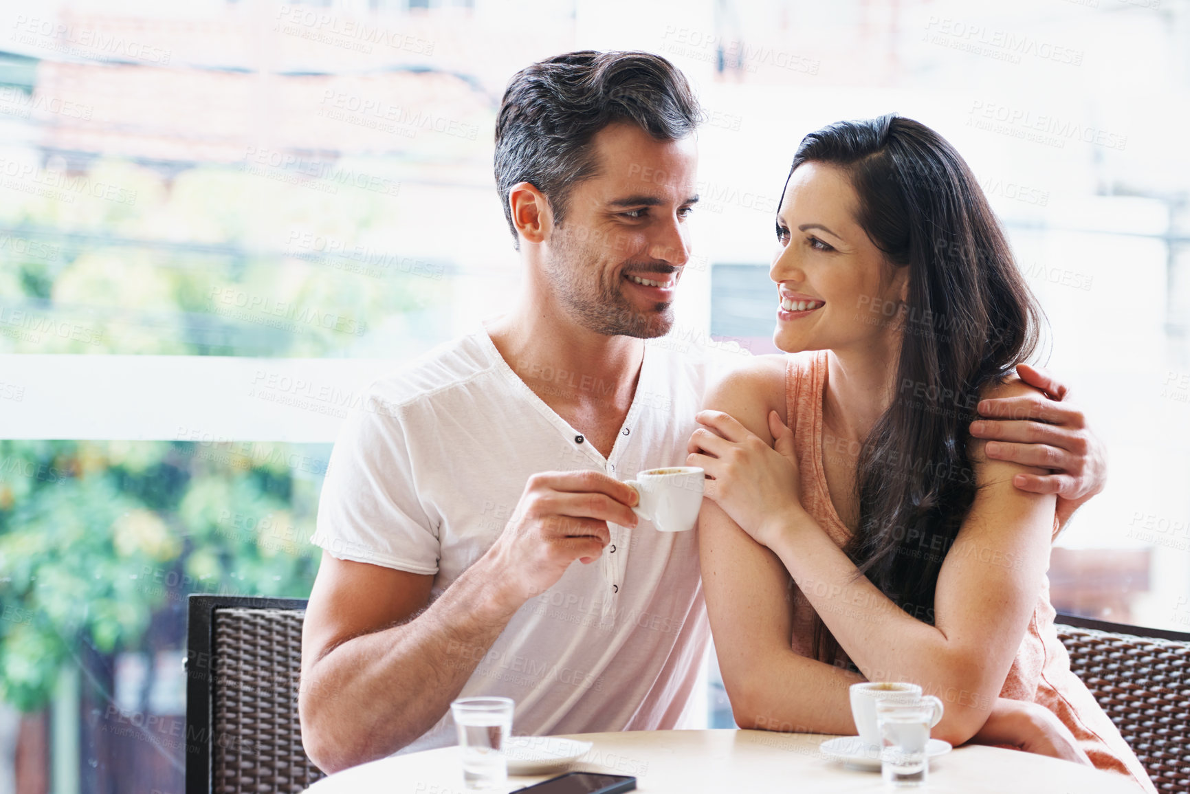 Buy stock photo Date, coffee and couple at cafe with happy, hug and love together with smile and hot drink at a table. Espresso, relax morning and marriage at a restaurant with bonding, care and romance on patio
