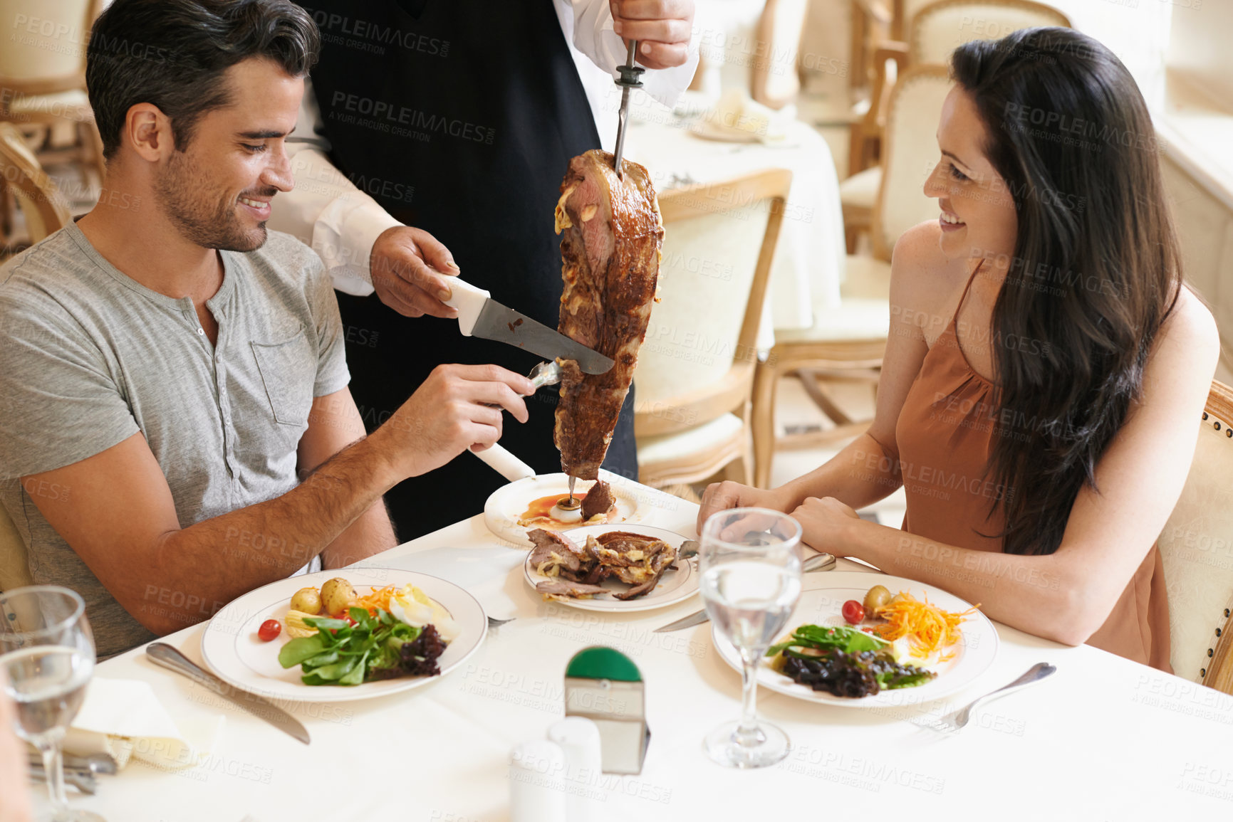 Buy stock photo Happy couple, date and waiter cutting kebab for serving, fine dinning or romantic dinner at table. Young man and woman with chef or skewer of food for meal, eating or enjoying service at restaurant