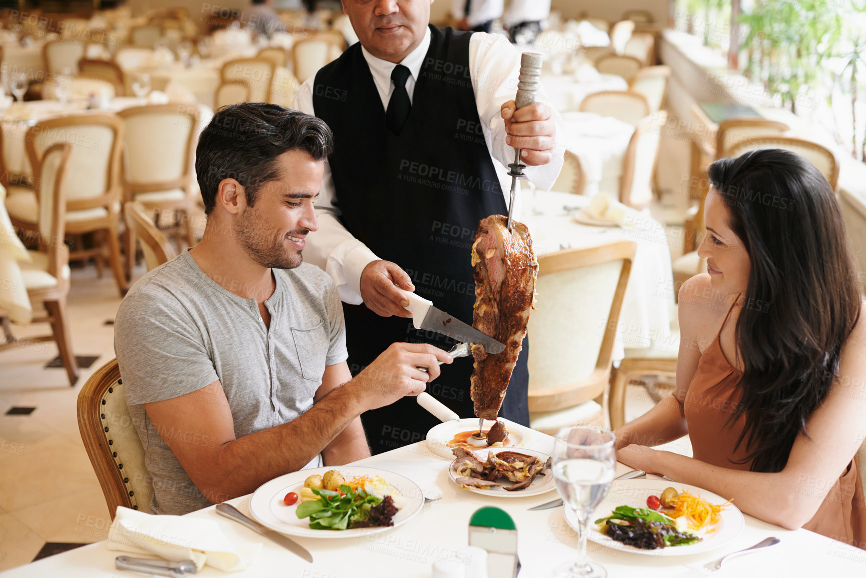 Buy stock photo Happy couple, date and dining with kebab of waiter serving, meat or slices on romantic dinner at table. Young man or woman with chef, skewer or food for meal, eating or enjoying service at restaurant
