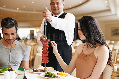 Buy stock photo Couple, fine dining and waiter serving food or sausage kebab on skewer or restaurant, anniversary or nutrition. Man, woman and relationship bonding dates in Italy with water carving, meal or eating
