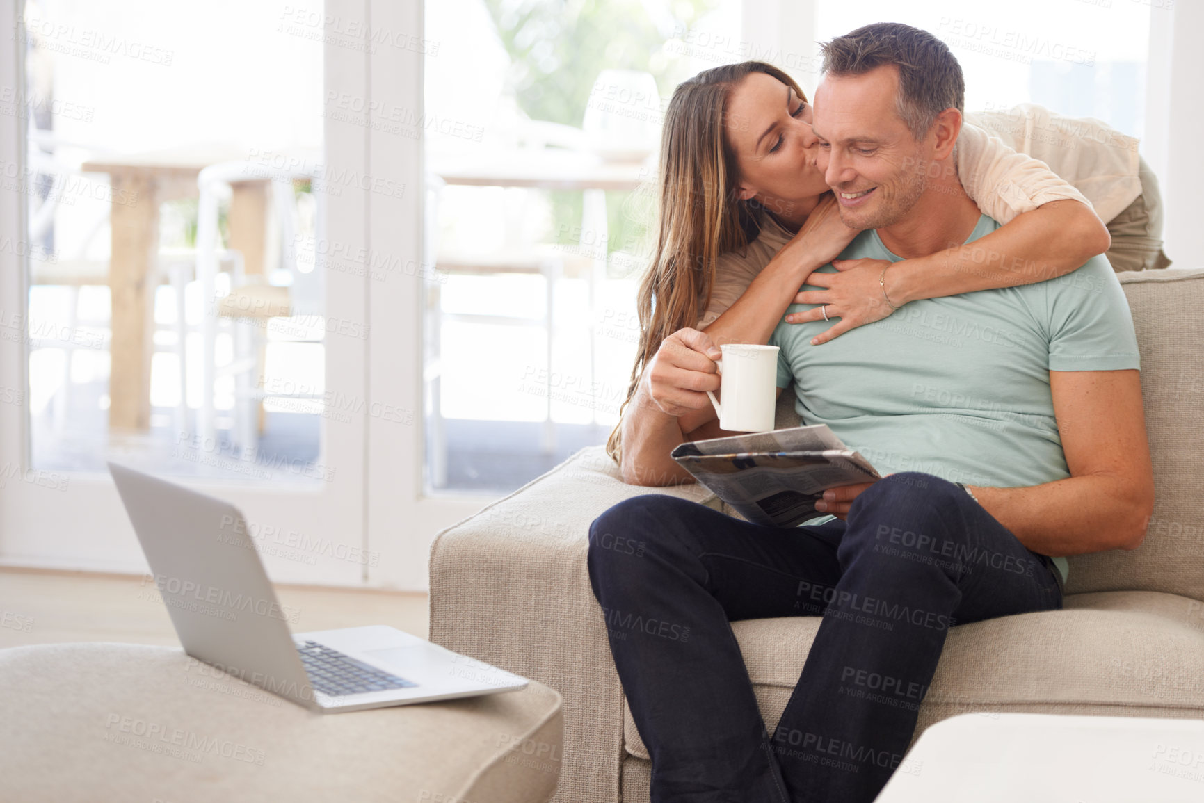 Buy stock photo Newspaper, hug and happy couple on sofa with love, kiss and affection at home for relaxing holiday or morning news. Mature woman with partner or people reading paper, laptop and drink coffee on couch