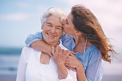 Buy stock photo Woman, kiss and senior mother at beach with happiness, love and smile for mothers day on vacation. Elderly lady, daughter and happy with hug, bonding and outdoor by ocean for holiday in retirement