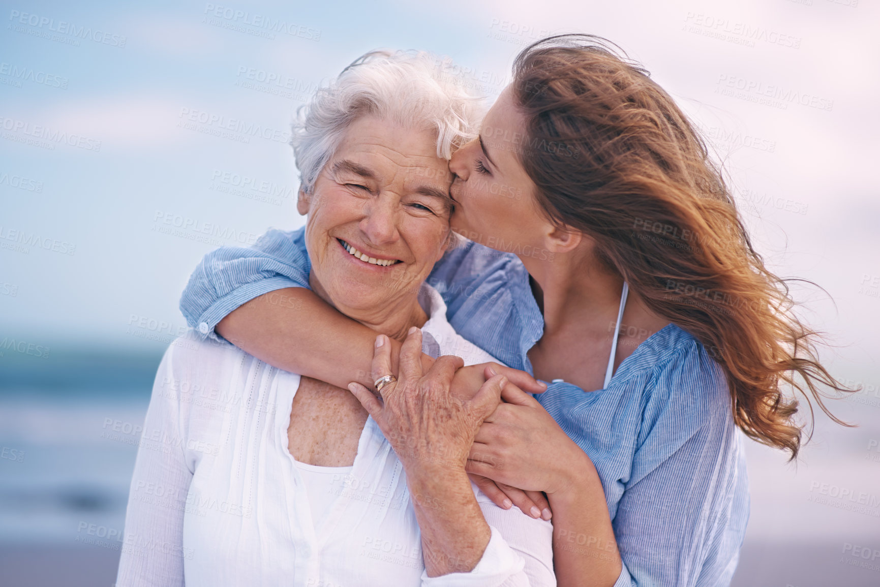 Buy stock photo Woman, kiss and senior mother at beach with happiness, love and smile for mothers day on vacation. Elderly lady, daughter and happy with hug, bonding and outdoor by ocean for holiday in retirement